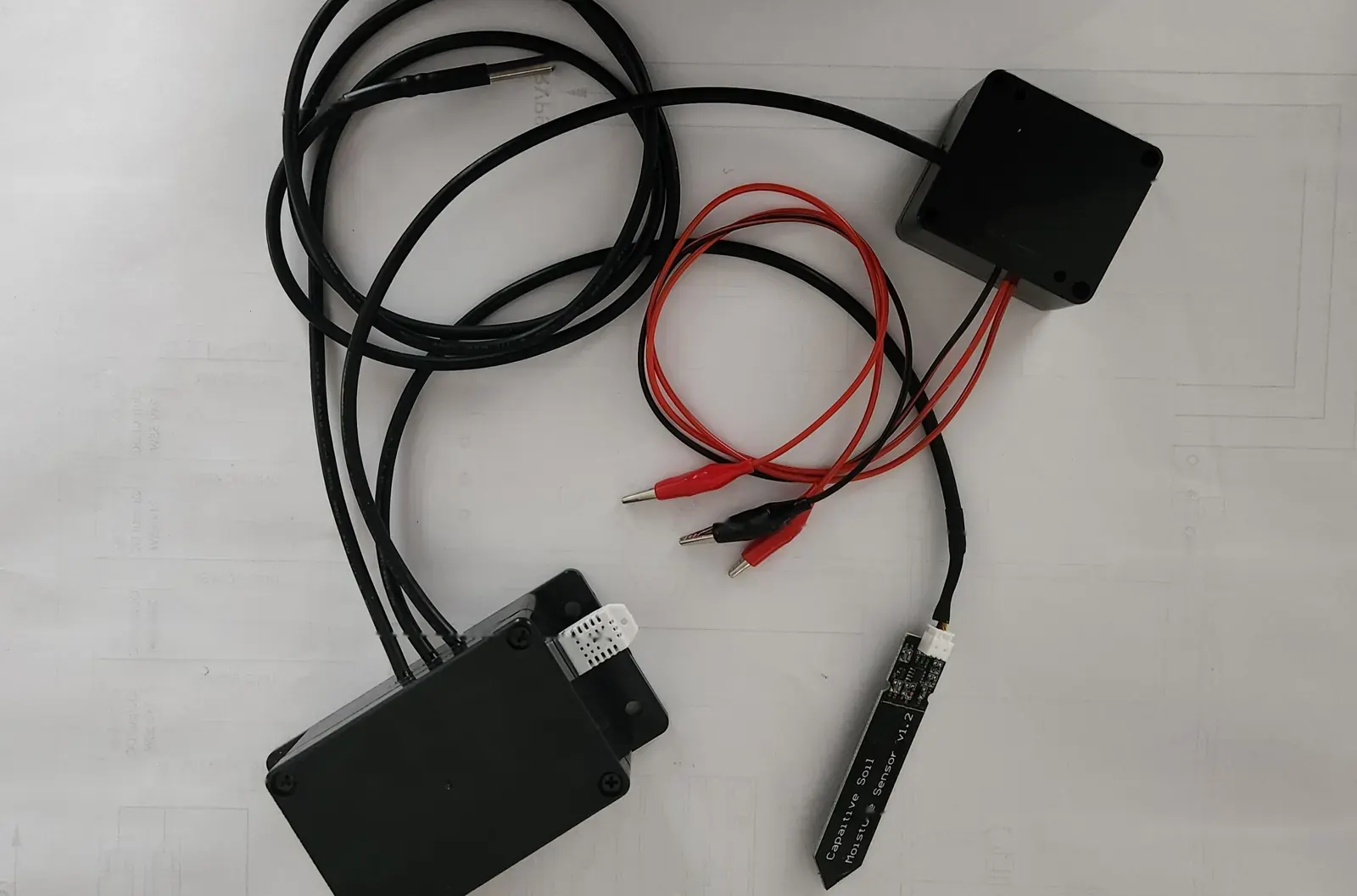 Prototype sensor unit laid out before deployment: two black enclosures, cables, electrode leads with clips, a stainless temperature probe and a soil moisture probe.